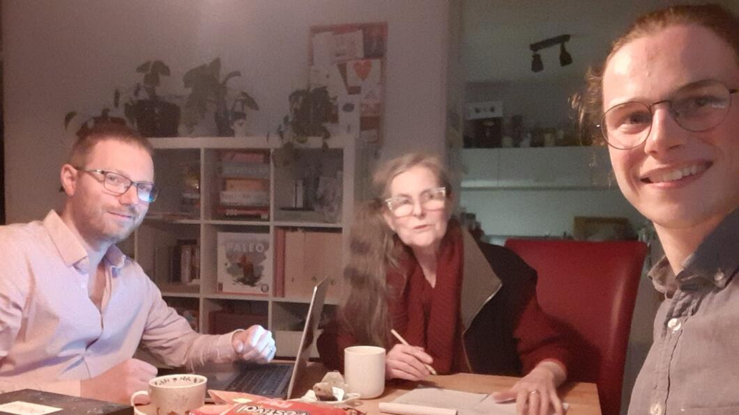 Drie mensen van verschillende leefitjden aan een tafel, met laptop en papieren voor zich. 