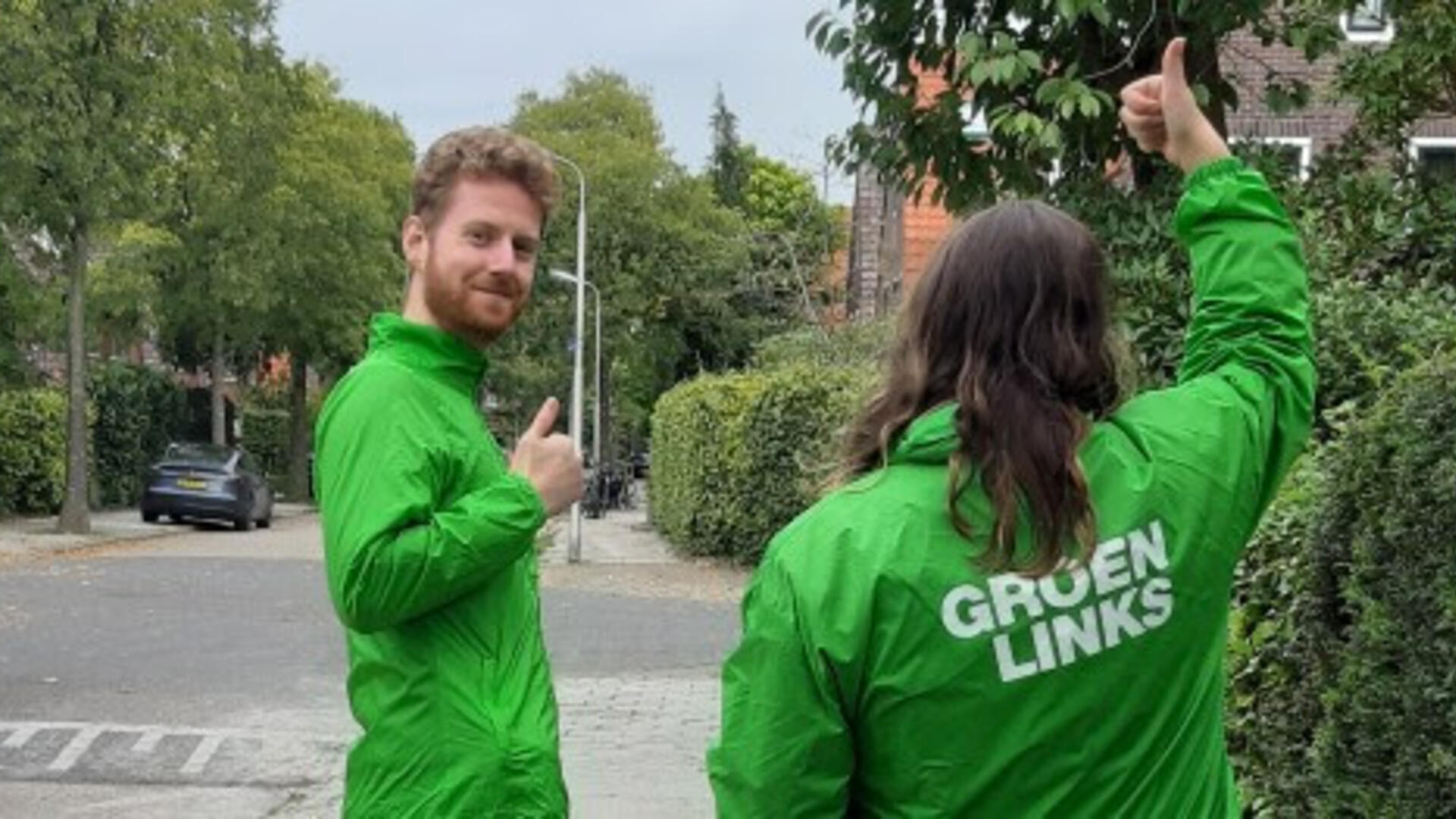 Een jongeman en een vrouw, beide met groen jasjes en tekst 'GroenLinks'op de rug. Beide steken een duim in de lucht. 